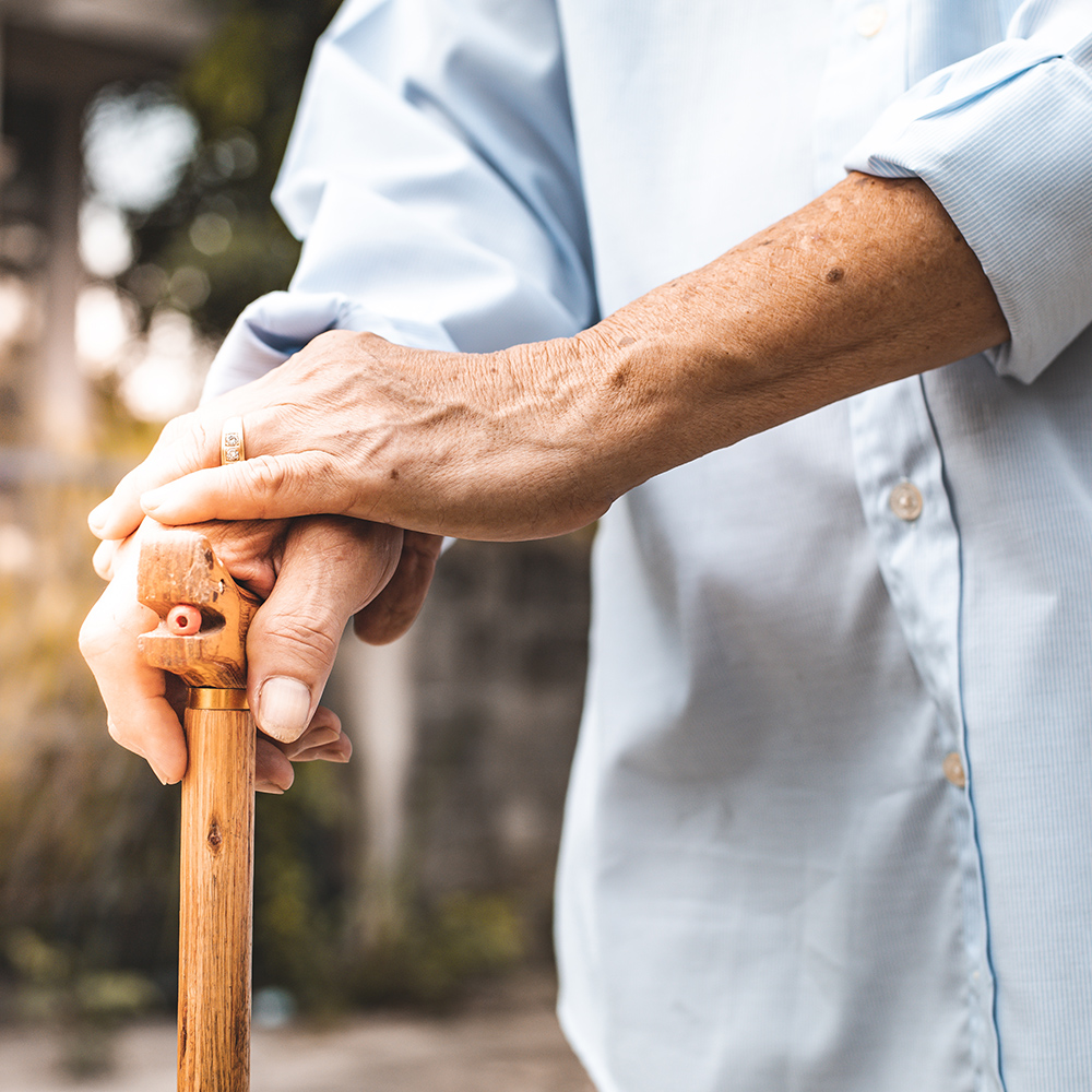 Close-up of an elderly person’s hands holding a wooden cane.